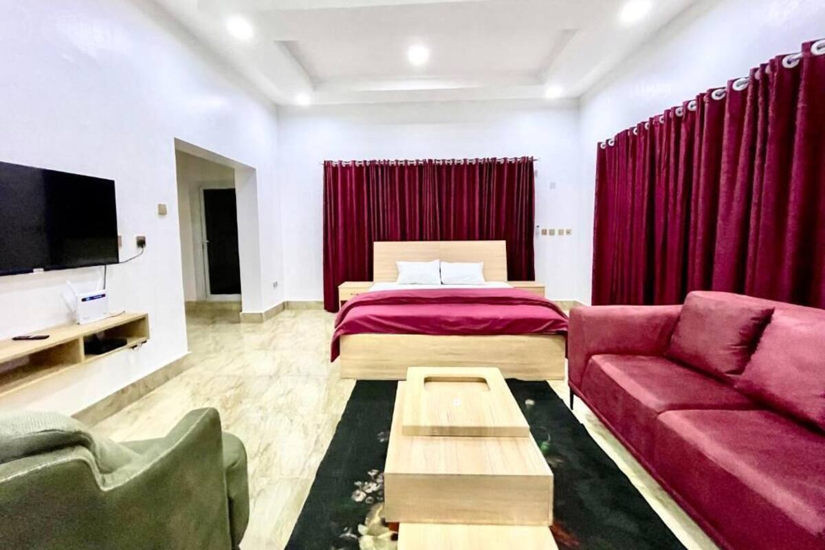 Camera d'albergo moderna con un letto, una TV, un divano rosso e un tavolino in legno.