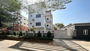 A modern building with multiple floors, a gated entrance, and a parking area with shadows cast by trees. - Marcopolo Hotel and Suites  (Lekki)