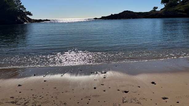 En strand med klart vand, sandet bredde og klippeformationer.