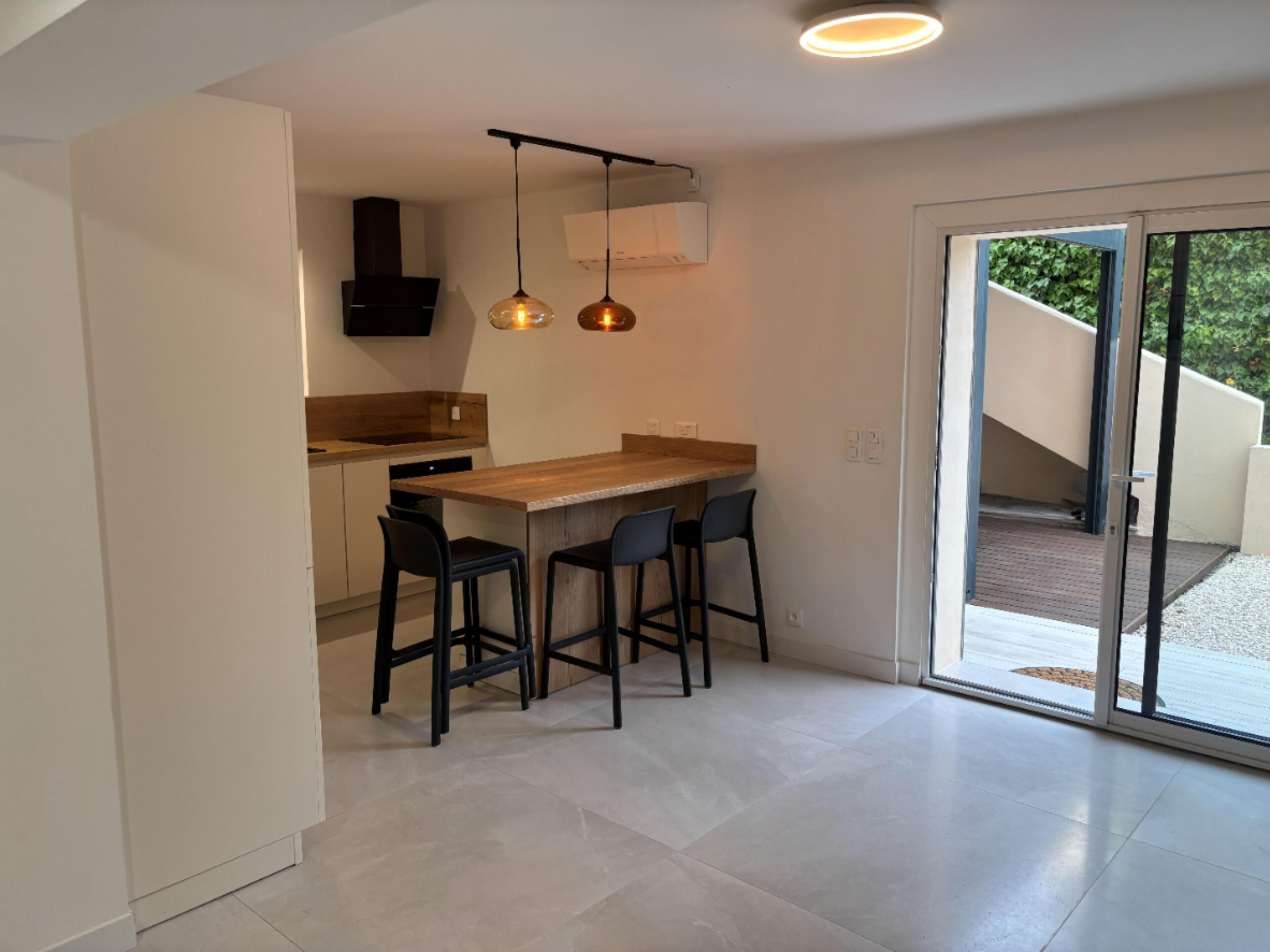 A modern kitchen with a wooden countertop, black bar stools, and pendant lighting.