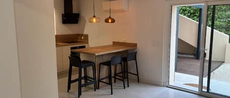 Una cucina moderna con piano di lavoro in legno, sgabelli da bar neri e illuminazione a sospensione.