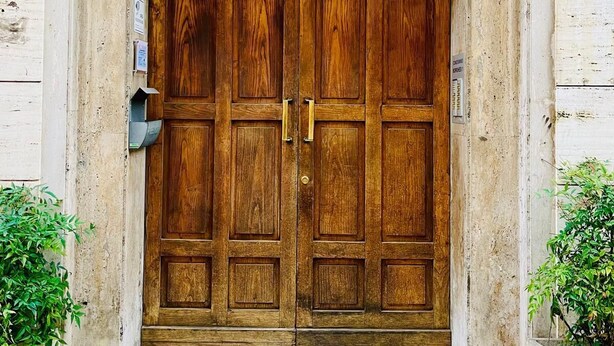 Een grote houten dubbele deur met een metalen handgreep, gelegen in een stenen muur met een klein opstapje.