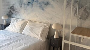 Een slaapkamer met een bed, twee nachtkastjes met lampen, een houten kledingrek en een wand met een marmerpatroon.