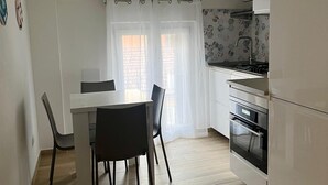 Een kleine keuken met een eettafel en stoelen, een witte koelkast en een betegelde achterwand.