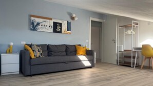 Een moderne woonkamer met een grijze bank, gele kussens, een witte bijzettafel en een schilderij aan de muur.