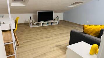 Un soggiorno moderno con televisore a schermo piatto, pavimento in legno, una poltrona gialla e un divano grigio con cuscino giallo.