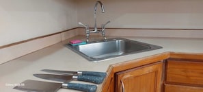 Una cocina con un lavaplatos de acero inoxidable, un armario de madera y dos cuchillos con mangos azules.