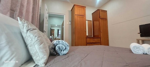 A bedroom with a bed, pillows, a wooden wardrobe, a mirror, and a TV.