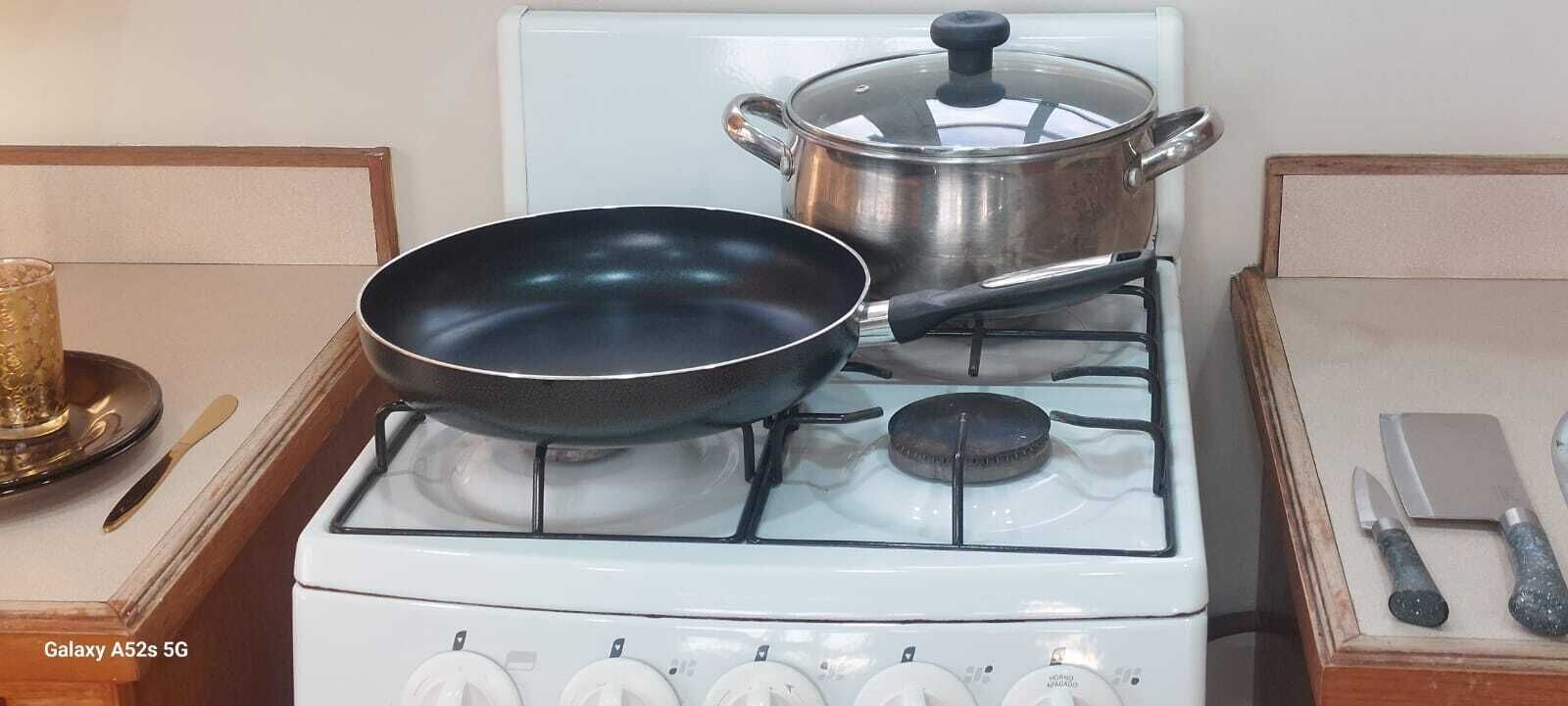 Una cucina con un fornello, una padella, una pentola e un set di coltelli sul piano di lavoro.
