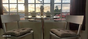 A room with a table and two chairs, a window with a view of buildings and a sunset.