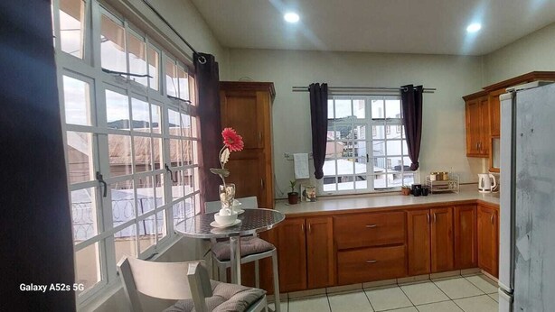 Eine Küche mit Holzschränken, einem Esstisch mit Stühlen, einem Fenster mit Vorhängen und einem Kühlschrank.