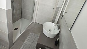 Ein modernes Badezimmer mit einer in Glas abgeschlossenen Dusche, einem weißen Waschbecken und einem dunklen Schminktisch.