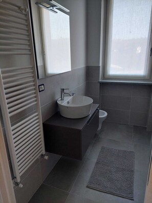 Une salle de bain moderne avec un lavabo rond, des toilettes et un porte-serviettes.