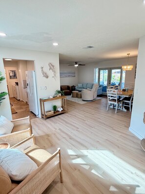 Ein geräumiger Wohnbereich mit Holzboden, einem Esstisch mit Stühlen, einer Couch und einem Deckenventilator.