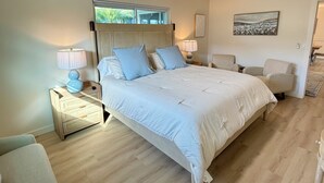 A spacious bedroom with a large bed, two bedside tables with lamps, a ceiling fan, and a view of the outdoors through a window. - Shar’s Cottage - Close to Beach - Bradenton (Bradenton)