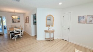 A spacious room with a dining area, a small table with chairs, a mirror, and a door. - Shar’s Cottage - Close to Beach - Bradenton (Bradenton)