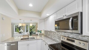 Una cucina moderna con mobili bianchi, ripiani in granito, elettrodomestici in acciaio inossidabile e illuminazione a sospensione.