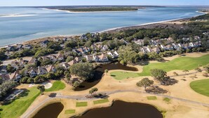 Vista aerea di una zona residenziale costiera con case, un campo da golf e una vasta distesa d'acqua.