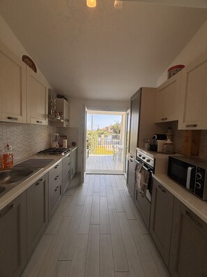 A modern kitchen with light-colored cabinets, a stainless steel sink, and a view to a balcony. - Wonderful two steps from the sea surrounded by greenery, reserved parking space. (Porto Ottiolu)