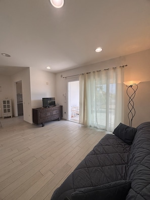 A spacious living room with a large sofa, a television on a wooden cabinet, and a sliding glass door leading to an outdoor area. - Wonderful two steps from the sea surrounded by greenery, reserved parking space. (Porto Ottiolu)