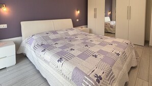 Makuuhuoneessa on suuri sänky, yöpöytä, vaatekaappi ja kaksi seinälle asennettua valaisinta.