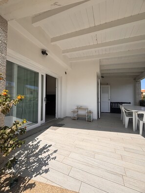 Un patio techado con mesa y sillas, una mesita con un florero y un banco.