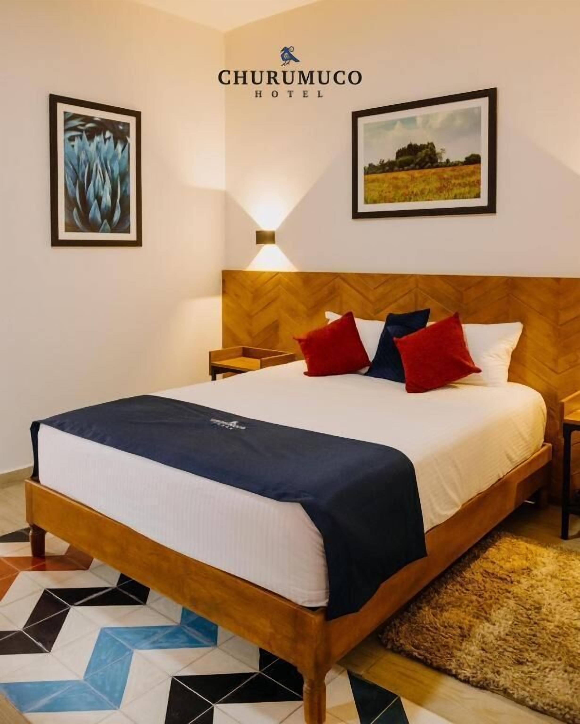 Habitación de hotel con una cama, mesitas de noche, un cabecero de madera y dos cuadros en la pared.