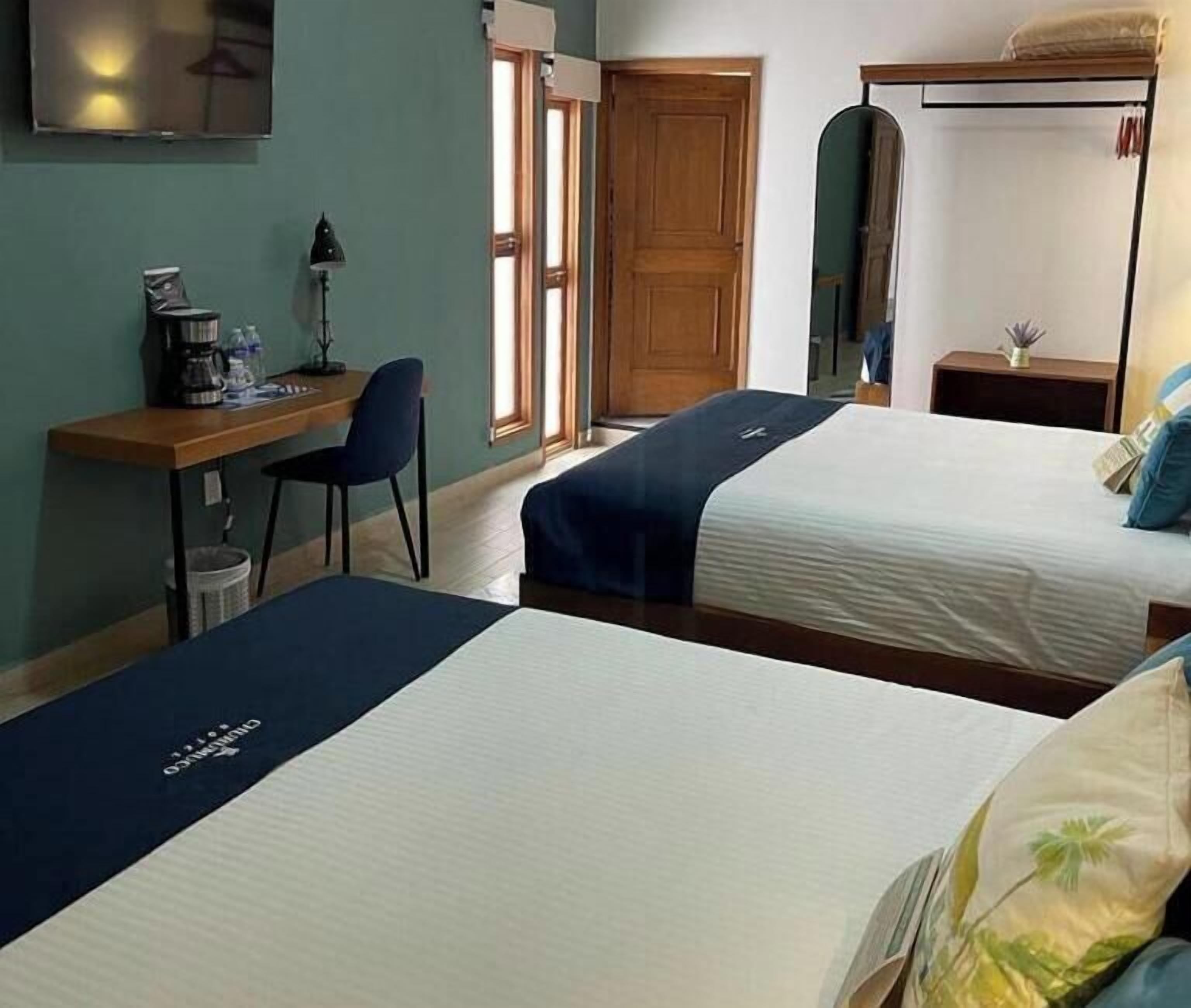 A hotel room with two beds, a desk, a chair, a mirror, and a window.