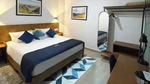Una habitación de hotel con cama, escritorio, silla, cafetera y espejo.