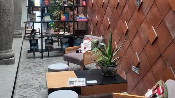 Un interior moderno con un diseño geométrico en la pared, zona de estar con sofá y sillones, una mesita y una planta en maceta.
