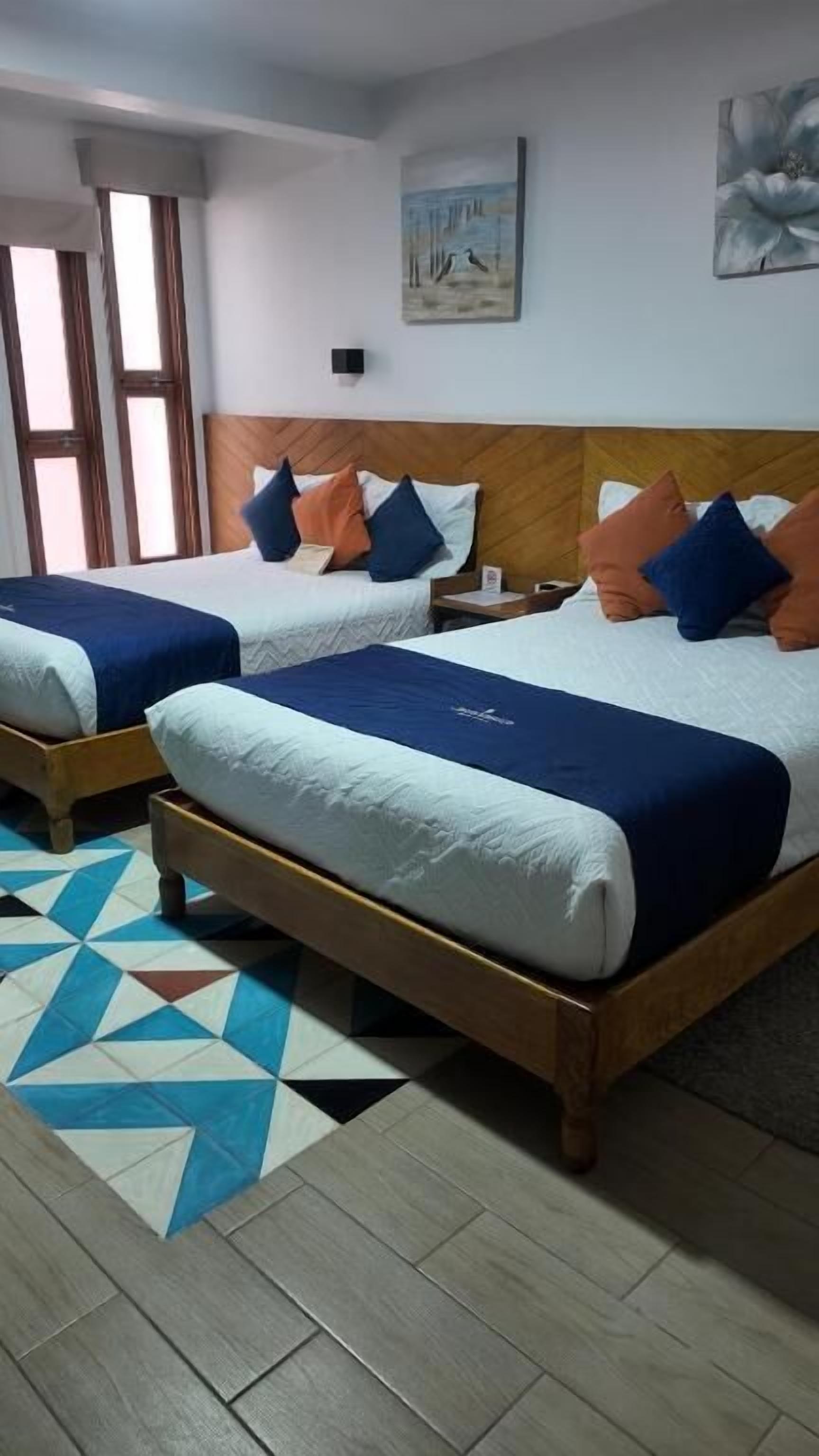 A hotel room with two beds, a wooden headboard, a patterned rug, and artwork on the walls.