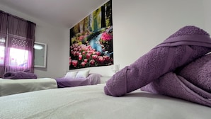A hotel room with two beds, each with a purple towel, a white bedspread, and a large floral painting on the wall. - Casa las Cordobesas is a charming rural lodging in the middle of nature. (La Guijarrosa (Córdoba))