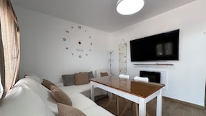 A modern living room with a white sofa, a wooden coffee table, a flat-screen TV mounted on the wall, and a fireplace. - Casa las Cordobesas is a charming rural lodging in the middle of nature. (La Guijarrosa (Córdoba))