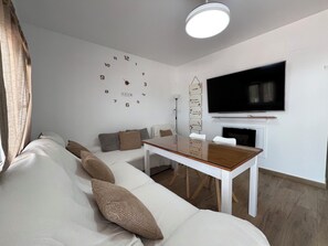 Ein modernes Wohnzimmer mit einem weißen Sofa, einem Holztisch, einem Flachbildfernseher an der Wand und einem Kamin.