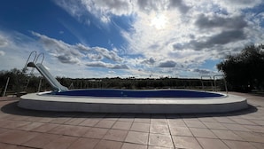 A swimming pool with a slide, surrounded by a tiled deck, under a partly cloudy sky. - Casa las Cordobesas is a charming rural lodging in the middle of nature. (La Guijarrosa (Córdoba))