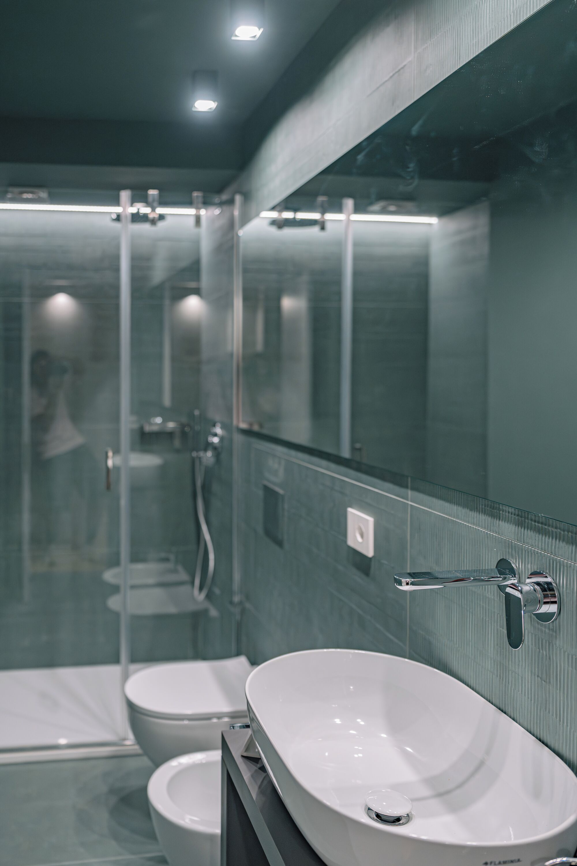 A modern bathroom with a glass shower enclosure, a white sink, and a toilet.