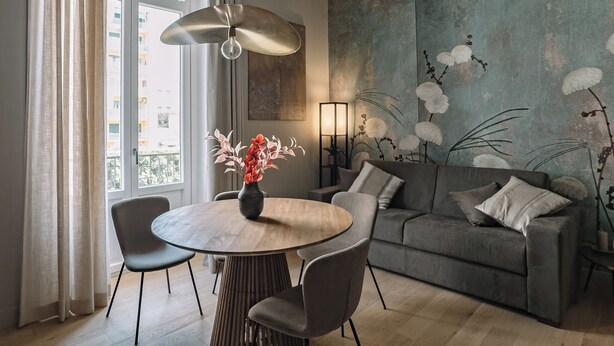 Ein modernes Wohnzimmer mit einem runden Esstisch, einem grauen Sofa und einem großen abstrakten Gemälde an der Wand.