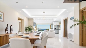 A modern dining area with a view of the sea, a wooden dining table, white chairs, and a white sofa in the background. - Villa Athena (Apokoronas)