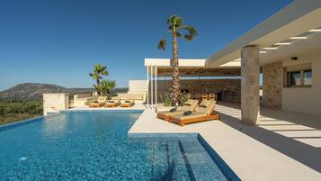 Una piscina al aire libre, sombrillas, sillones reclinables de piscina