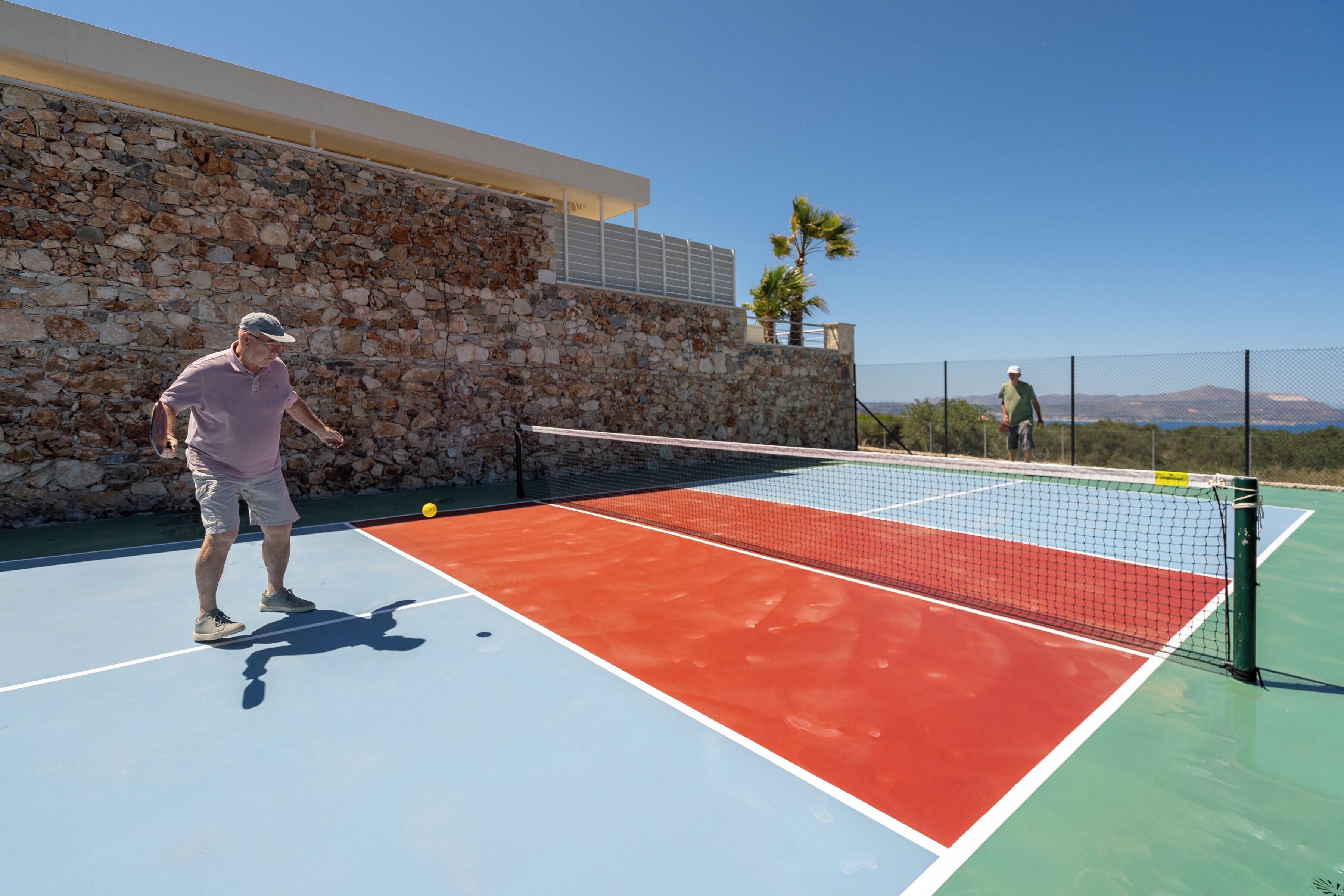 Un court de tennis en plein air, avec un mur en pierre et un ciel dégagé.