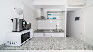 A compact kitchen with white cabinets, a microwave, a kettle, and a sink. - Apartamentos Monte Verde (Mogán)