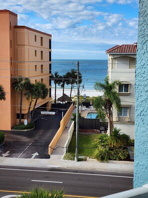 On voit un bâtiment situé en bord de mer, avec une route dégagée menant à la plage, des palmiers et un panneau indiquant une hauteur libre de 1,80 mètre.