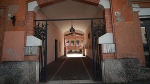 Una entrada arqueada con fachada de ladrillo, puertas de metal y un camino que conduce a un edificio con ventanas y una puerta.