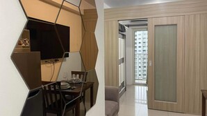 Ein modernes Wohnzimmer mit Essbereich, einem an einer Wand mit geometrischem Muster montierten Flachbildfernseher, einer Glasschiebetür, die auf einen Balkon führt, und Blick auf ein Hochhaus.