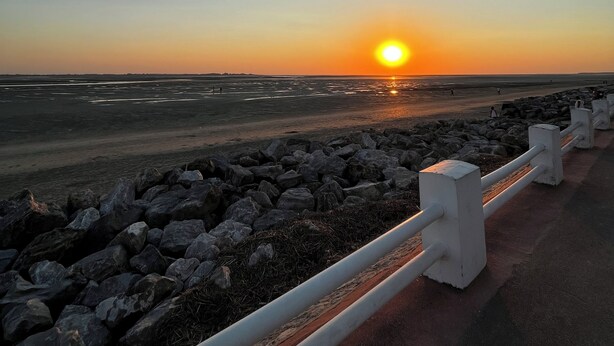 A sunset over a beach with a rocky shoreline and a white railing. - COTTAGE L'OUSTAL ideally located beach and seawall 100 meters away (Le Crotoy)
