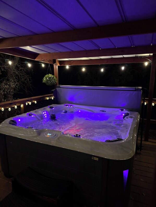 A hot tub with a wooden deck and string lights.