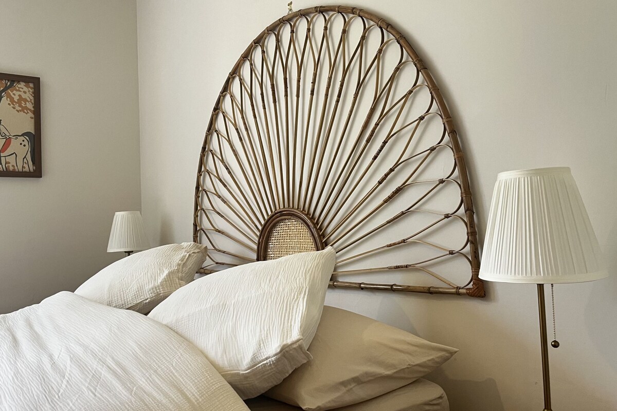 A bed with white bedding, a wall-mounted decorative headboard, a framed picture, and a floor lamp.