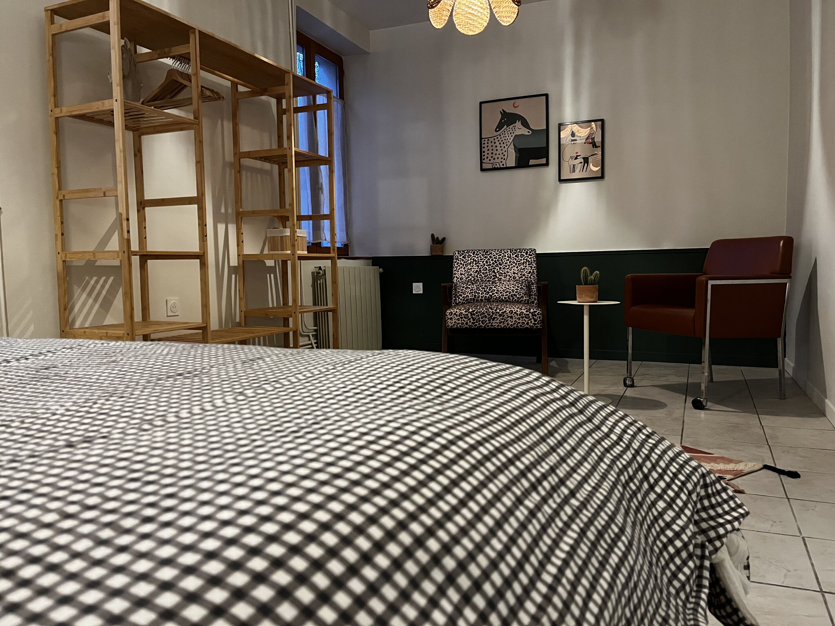 A bedroom with a bed, a wooden wardrobe, a chair, a small table, and two wall art pieces.