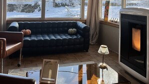 Een gezellige woonkamer met een donkerblauwe bank, een glazen bijzettafeltje en een open haard.