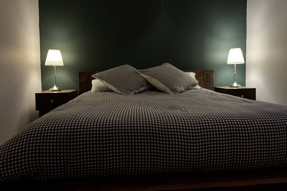 A bed with a checkered bedspread, two bedside lamps, and a dark wall.